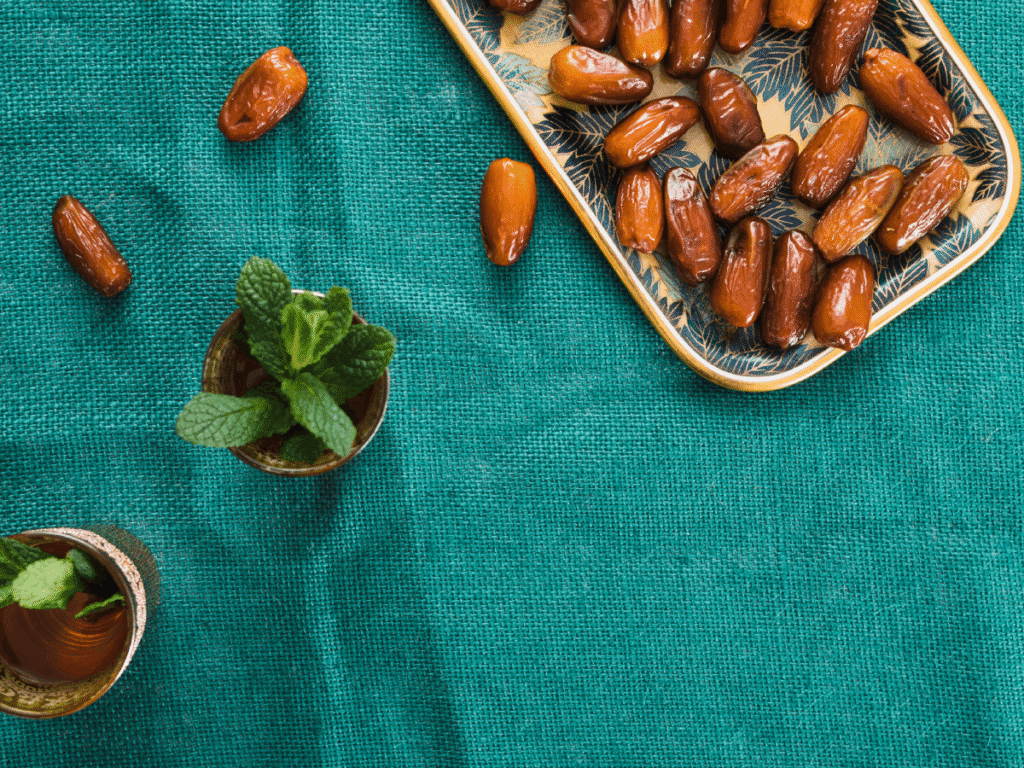 Top-down view of glossy dates arranged on a patterned tray alongside mint tea cups on a vibrant green fabric—illustrating a refreshing and energy-boosting summer snack setup.